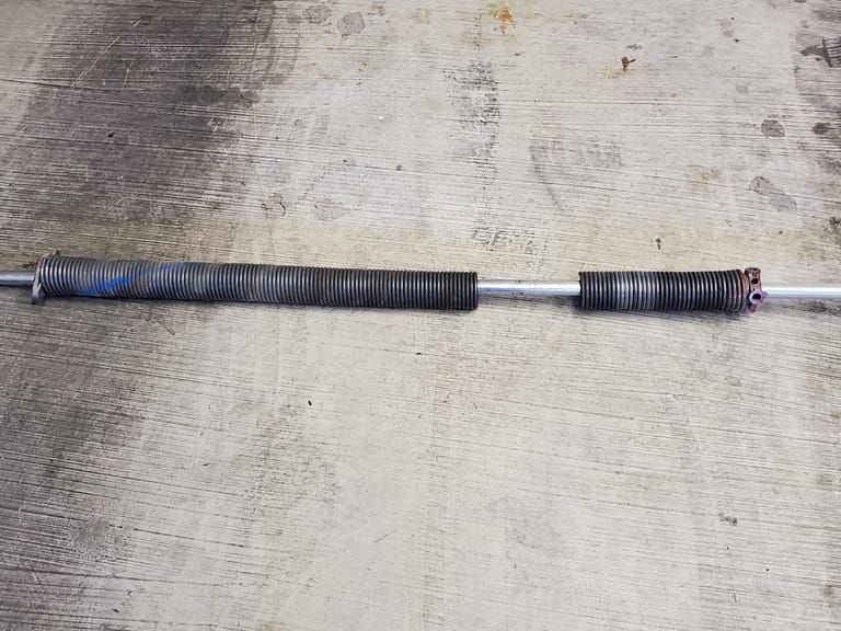 A garage door torsion spring snapped in two on a concrete shop floor.