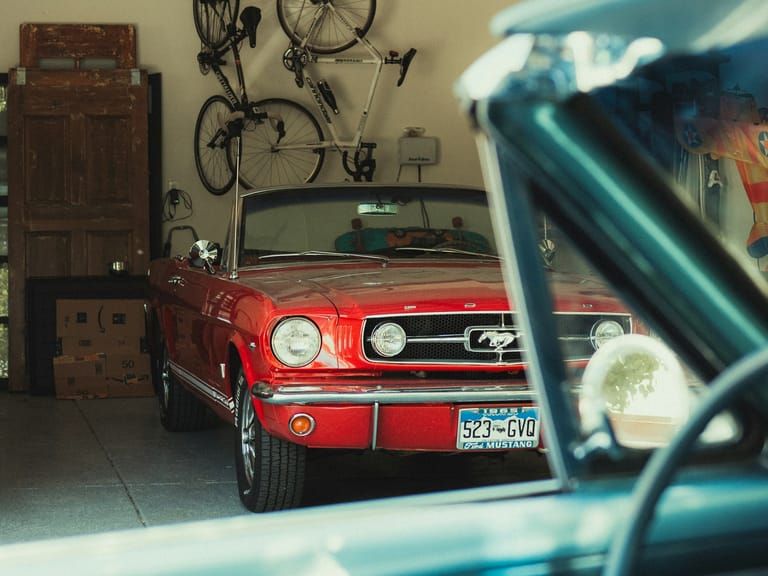 A red car parked inside a home garage, the opener rail overhead.