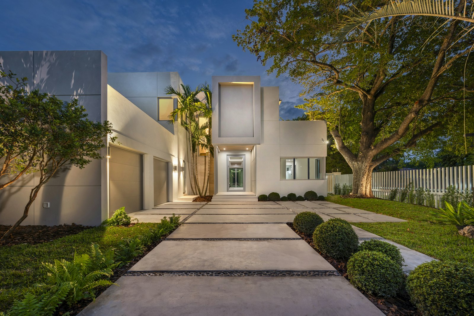 A modern home at dusk, walkway lights on, garage door closed for the night